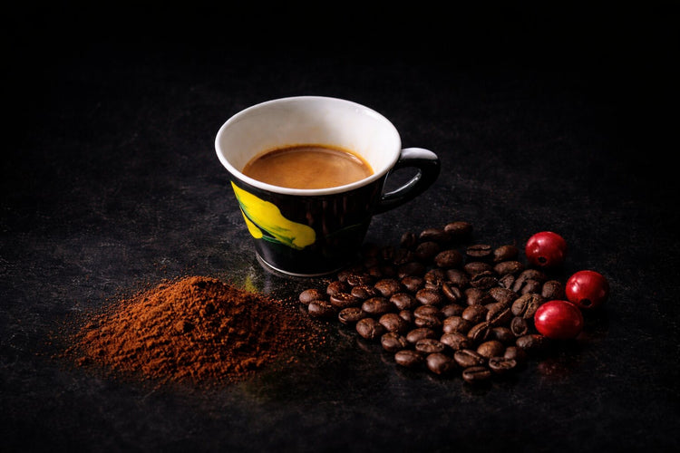 Espresso in der Tasse, daneben geröstete Bohnen und Kaffeekirschen